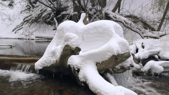 Panning over logs lying in river covered in fresh snow