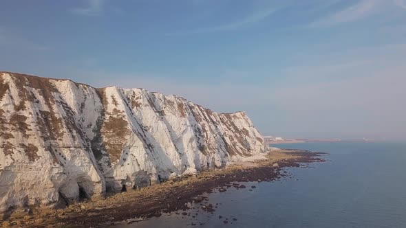 Drone flies low towards the White Cliffs of Dover with camera panning right. Beautiful turquoise sea