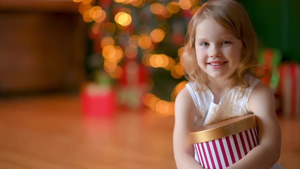 Happy Cute Girl with a gift in her hands sits in a cozy room