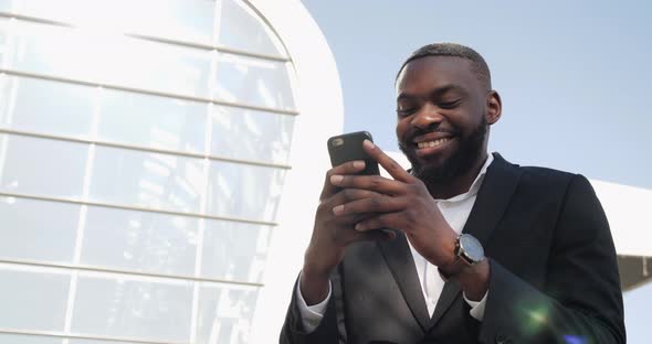 Handsome African-American Businessman is browsing his Smartphone, smiling Charmingly.