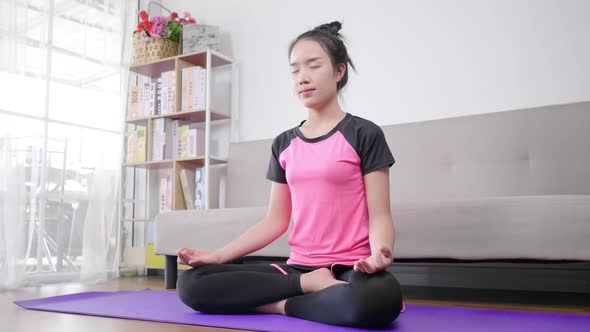 Asian woman doing meditation and sitting in lotus pose on yoga mat