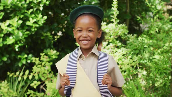 Animation of african american girl in scout costume smiling at camera in garden