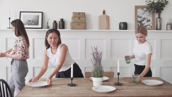 Three women are standing in the kitchen laying out plates for a joint dinner