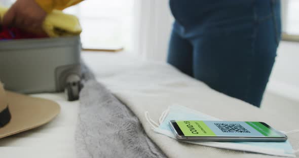 African american plus size woman packing suitcase with covid passport on smartphone