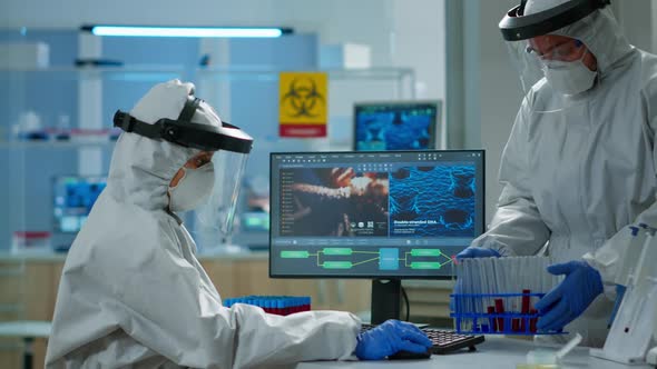 Biologist Doctor in Ppe Suit Checking Liquid Sample Typing on Pc