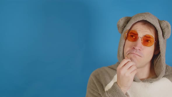 Man in Sunglasses and Hoodie with Ears Thoughtfully Looks Away on Blue Background with Space for