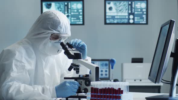 Scientist in protection suit and masks working in research lab using laboratory equipment.