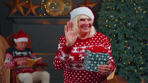 Senior Grandmother in Christmas Sweater Smiling Friendly at Camera and Waving Hands Gesturing Hello