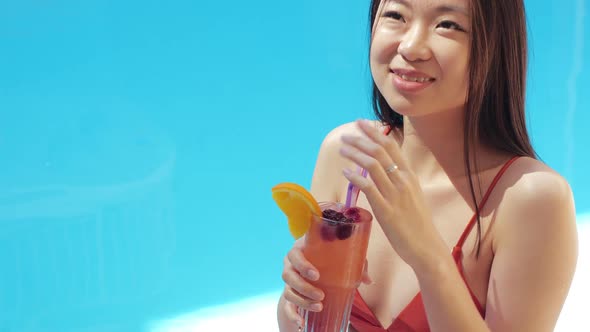 Portrait of Joyful Asian Woman in Glasses Sitting Poolside Outdoors Drinking Cocktail Smile Looking