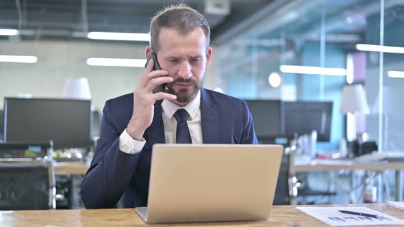 Upset Young Businessman Talking on Smartphone