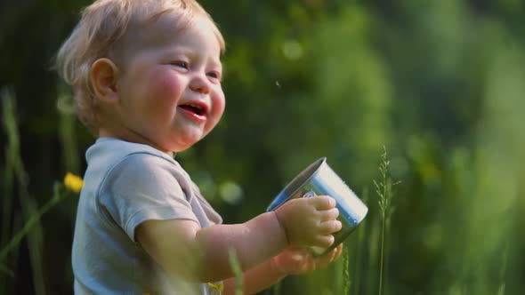 one year old baby spills liquid from a metal mug. The concept of walking outdoors,