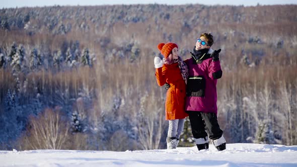 Happy Young Coulple Waving Hands to Camera in Mountain Ski Resort at Sunny Day