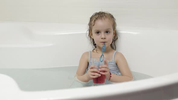 Cute Blonde Girl Takes a Bath in Swimwear and Drinking a Cocktail. Little Child
