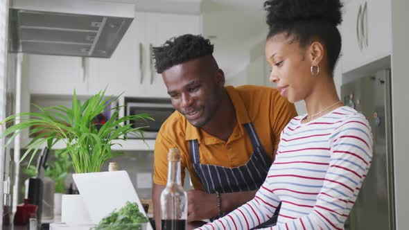 Video of happy african american couple cooking together in kitchen with tablet