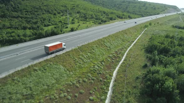 Drone Following Slow Driving Red Cargo Truck on Highway with Green Hills