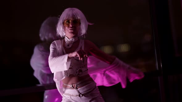 A Beautiful Blonde in a Sexy White Suit Makes Dance Moves Standing Isolated Against a Dark