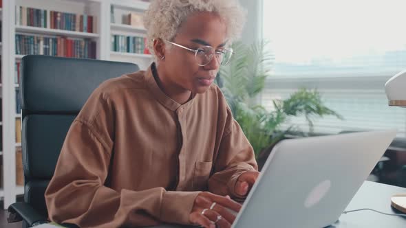 Young African American Woman Working with Laptop Typing Article Sits in Office
