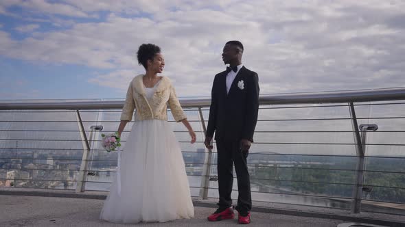 Cheerful African American Bride and Groom Jumping Up in Slow Motion on Bridge