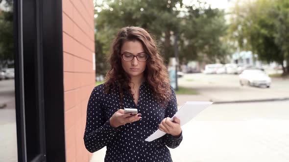 Young Beautiful Business Woman Walking in the City with Documents and Talking on the Phone