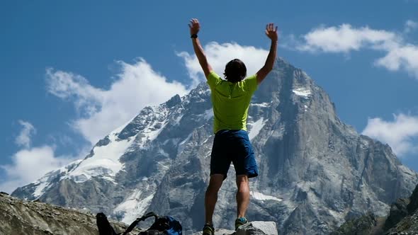 Man Raises Hand Up in the Mountains in a Hike Standing on a Stone, a Beautiful View Opens Up