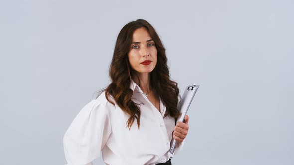 Female Entrepreneur in White Shirt is Holding Black Clipboard with Sheets Looking at you Winking and