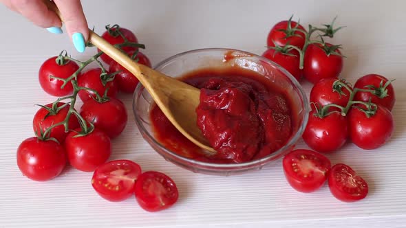 Closeup of a Woman Puts a Wooden Spoon in Tomato Paste on a White Background