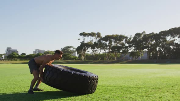 Fit shirtless caucasian man exercising outdoors with tire
