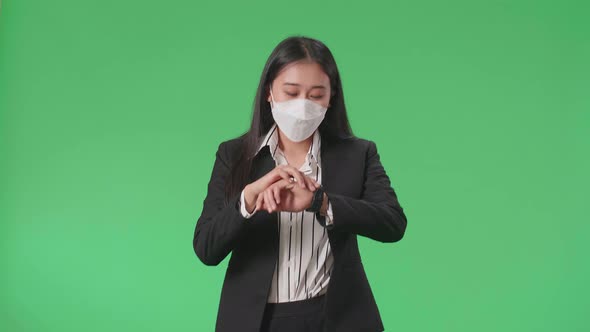 Asian Business Woman Wearing Mask Looking At A Watch While Walking On Green Screen Studio