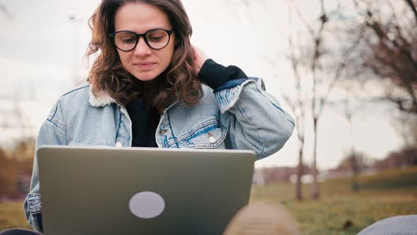 Young Woman Typing on Her Laptop While Sitting on the Lawn in the Park