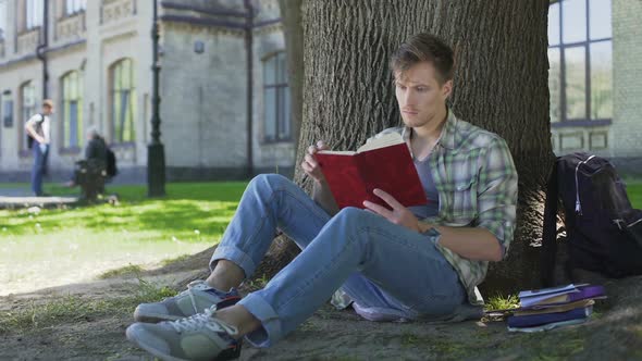 Male student skimming through pages of textbook, repeating learned material
