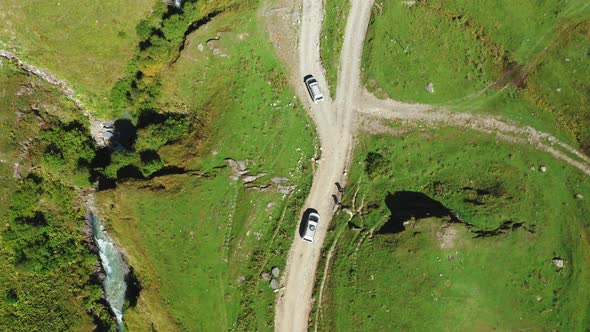 A Topdown Aerial View of of Two Cars of Travelers Driving Along a Dirt Road One After the Other