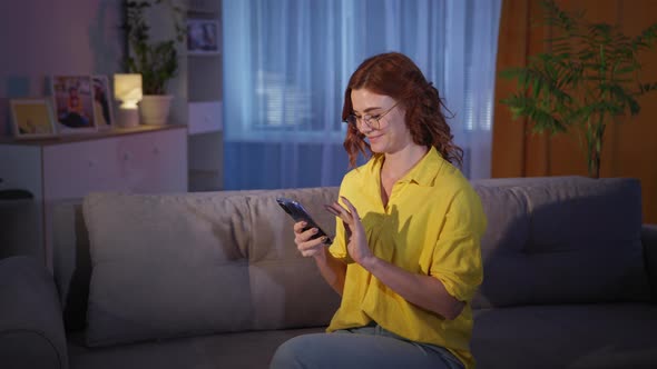 Woman in Glasses Makes Purchases on Internet on Her Smartphone While Sitting on Couch at Home Shows