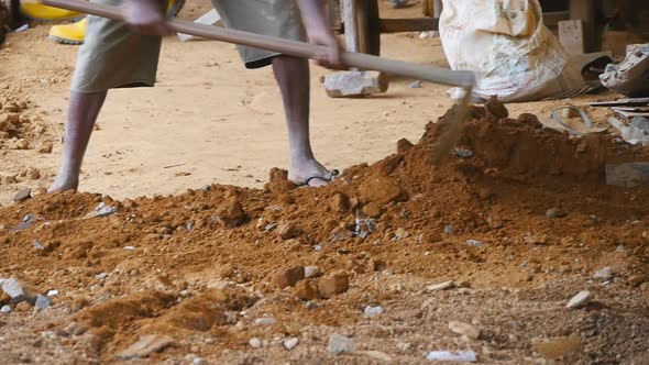 Low View of Male Indian Hands Rakes Sand or Ground with a Hoe at Building Site. Local Unrecognizable