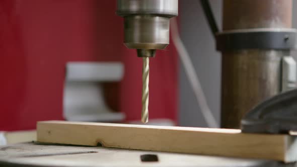 UHD close up of a drill press slowly drilling through a small piece of wood