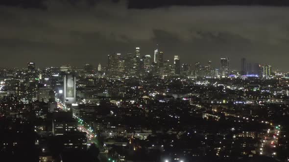 AERIAL: Over Dark Hollywood Los Angeles at Night with Clouds Over Downtown and City Lights 