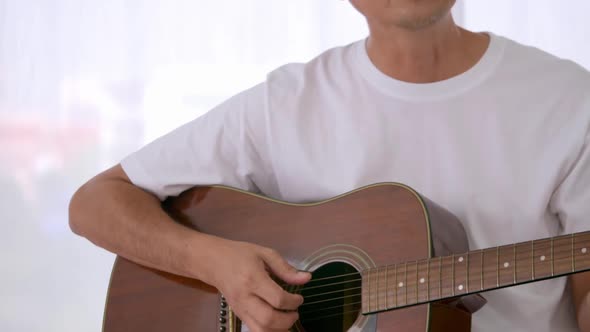 Happy Asian man playing guitar at the bedroom.