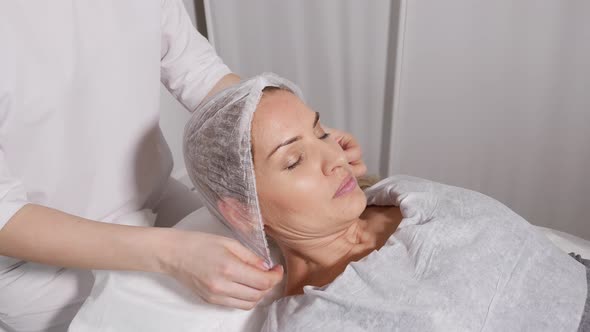 Doctor Beautician Wears a Cap Patient Before the Procedure Lying