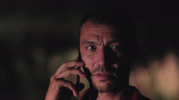 Concerned Young Man Speaks on the Phone at Night in the Forest