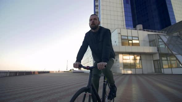 Stylish Handsome Man Riding Bicycle During Sunset or Sunrise with Sea Port on Background