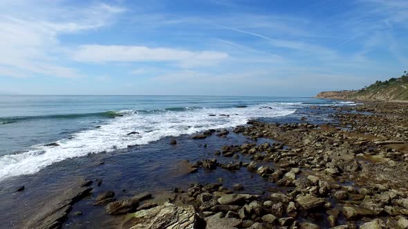 Tracking shot of a young man running on a rocky ocean beach shoreline