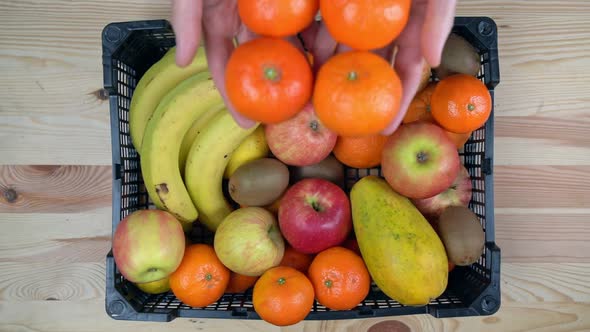 A Man Throws Tangerines on a Box of Tropical Exotic Fruits in Slow Motion