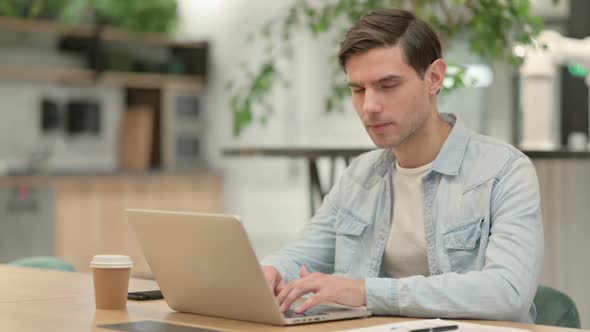 Creative Young Man Looking at Camera While Using Laptop in Office
