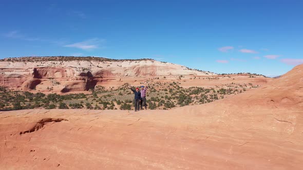 Drone Flies Away From Two Tourists Waving Their Arms And Stand In Arch Of Rocks