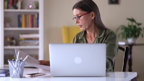 Old Mature Business Woman Freelancer Working on Laptop and Analyzing Paper Document Spbi