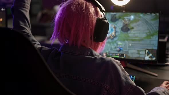 Back View of an Unrecognizable Pinkhaired Woman with Headphones Looking at a Computer Screen During