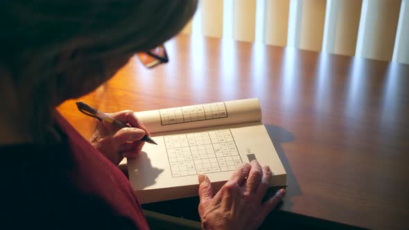 Middle aged caucasian woman with aging hands solving a number puzzle book for mind acuity to stay me