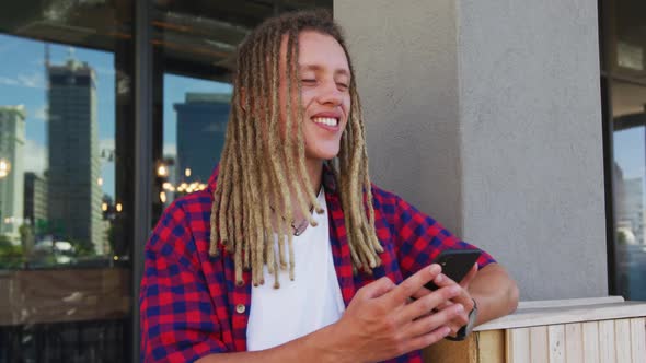 Mixed race man with dreadlocks sitting at table outside cafe using smartphone