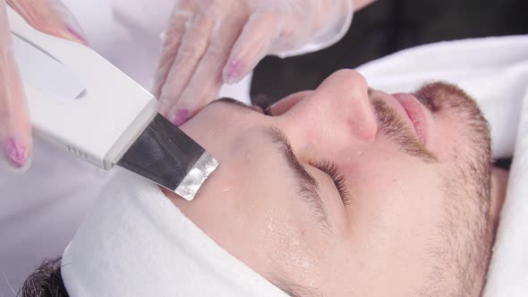 Ultrasonic Face Scrubber. Beautician Cleans the Face of a Young Man