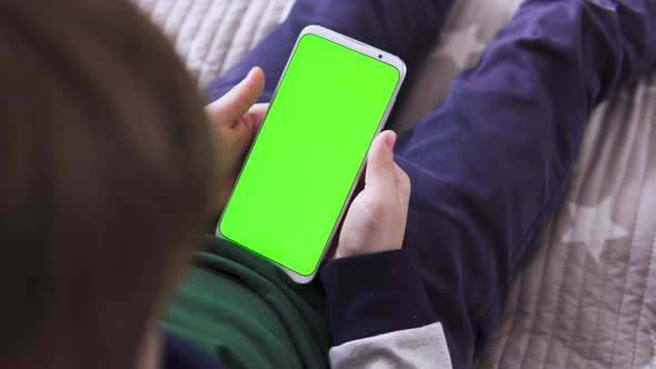 The Child Is Holding a Smartphone in Hand with a Green Screen for Keying Playing a Game Top View