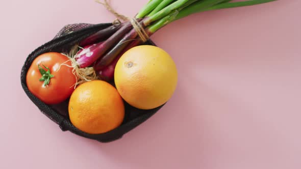 Video of fresh fruit and vegetables in black bag over pink background